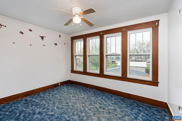 unfurnished room with baseboards, a healthy amount of sunlight, dark colored carpet, and ceiling fan