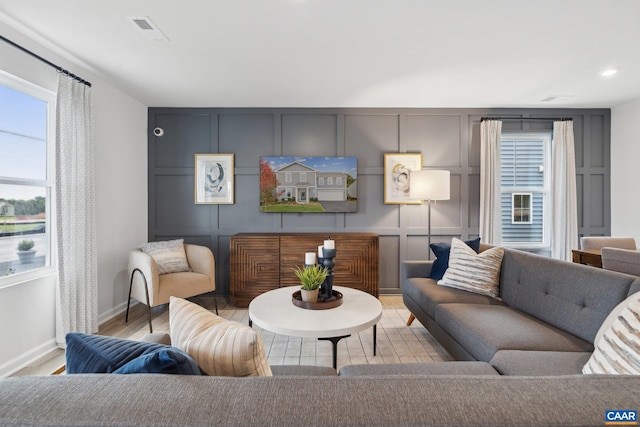 living room featuring baseboards, a decorative wall, visible vents, and wood finished floors