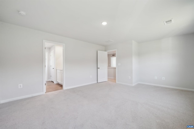 unfurnished bedroom featuring baseboards, light carpet, connected bathroom, and visible vents