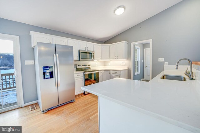 kitchen with sink, white cabinetry, stainless steel appliances, vaulted ceiling, and kitchen peninsula