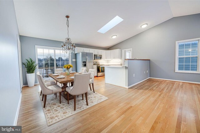 dining area with vaulted ceiling with skylight, a chandelier, and light hardwood / wood-style flooring