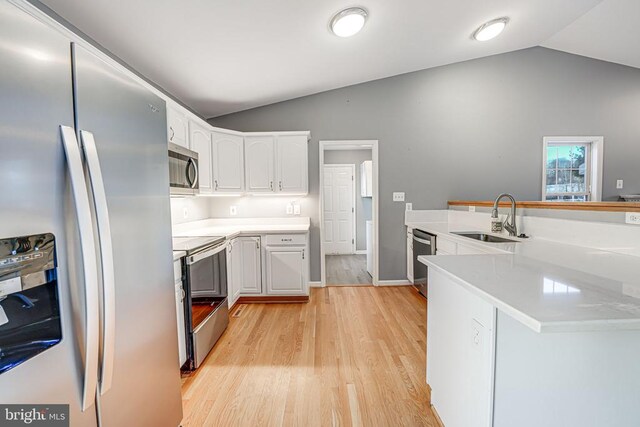 kitchen with vaulted ceiling, appliances with stainless steel finishes, white cabinetry, sink, and kitchen peninsula