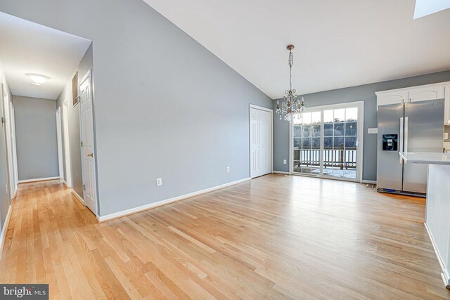 unfurnished dining area with lofted ceiling, a chandelier, and light wood-type flooring