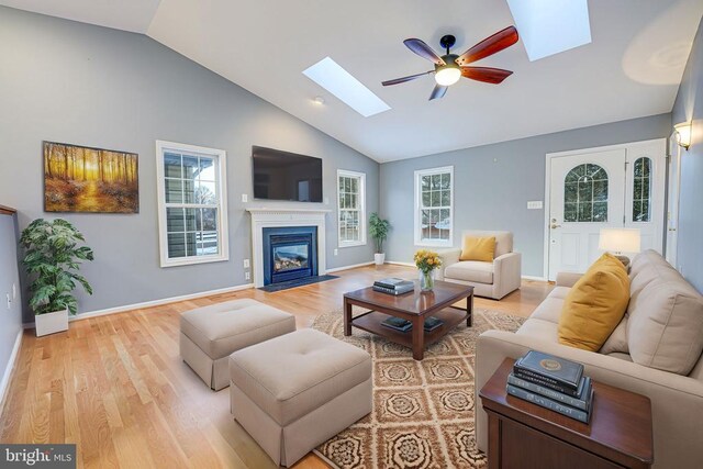 living room featuring ceiling fan, a skylight, high vaulted ceiling, and light wood-type flooring