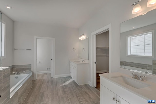 bathroom featuring a bath, a walk in closet, two vanities, and a sink