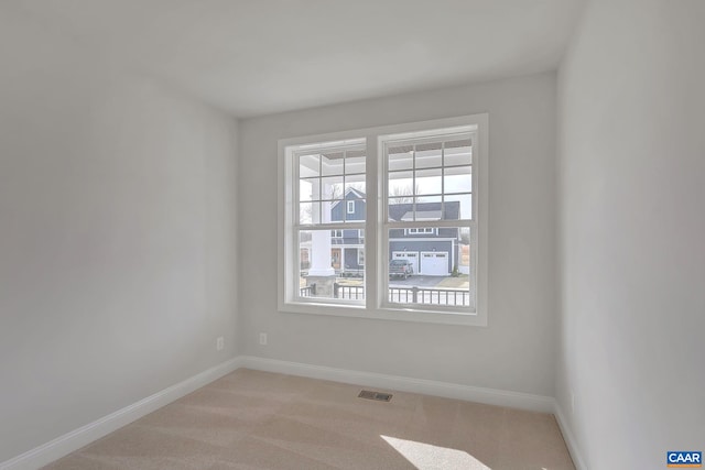 empty room featuring light colored carpet, a wealth of natural light, baseboards, and visible vents