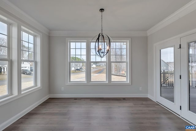 unfurnished dining area with an inviting chandelier, ornamental molding, a wealth of natural light, and dark wood-type flooring