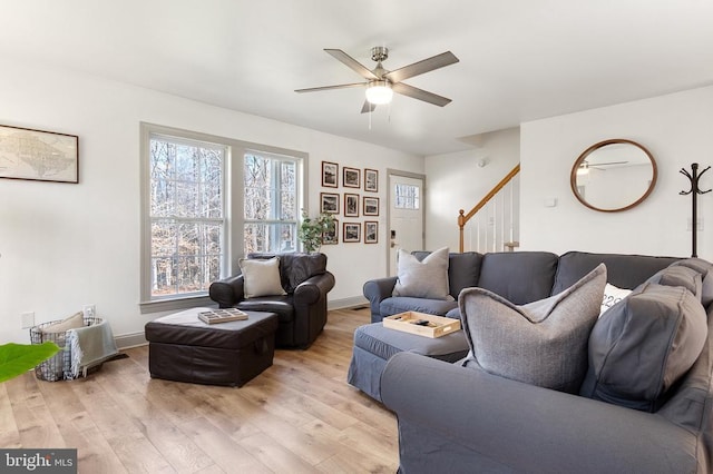 living area featuring light wood-style flooring, stairs, baseboards, and a ceiling fan