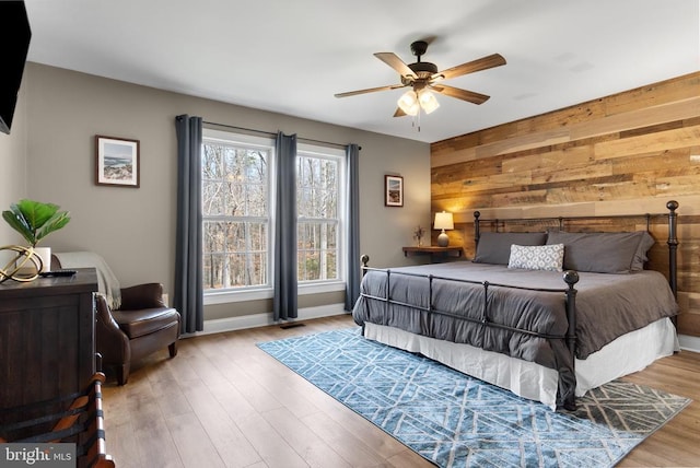 bedroom with wooden walls, light wood-style flooring, baseboards, and a ceiling fan