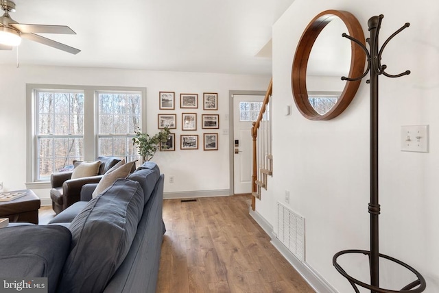 living room with baseboards, visible vents, ceiling fan, wood finished floors, and stairs