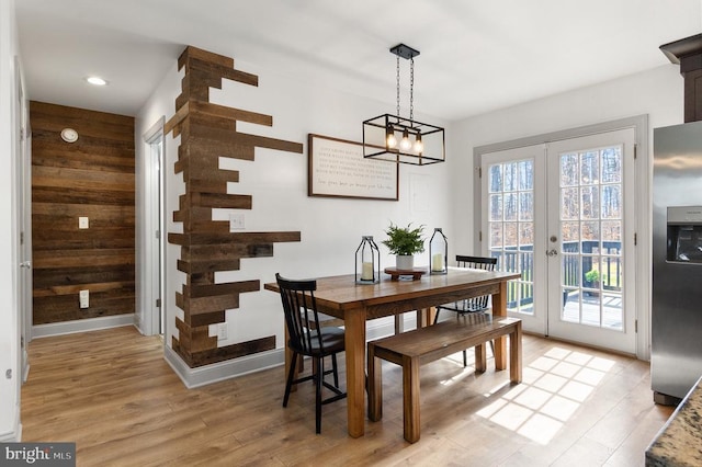 dining room with french doors, wood walls, light wood-style flooring, and baseboards