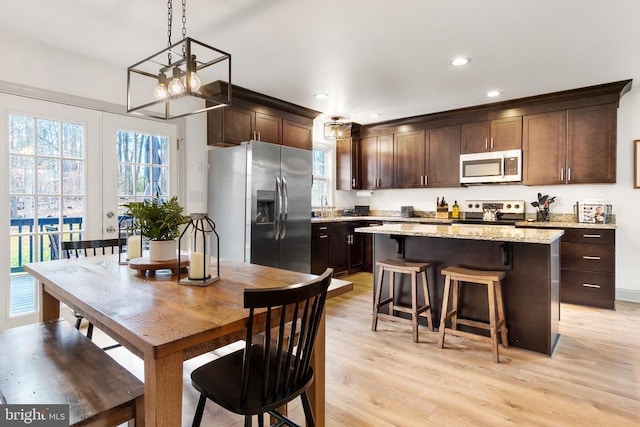 kitchen featuring a center island, hanging light fixtures, light stone countertops, stainless steel appliances, and dark brown cabinets