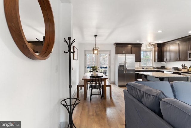 kitchen featuring stainless steel fridge with ice dispenser, light stone counters, open floor plan, dark brown cabinets, and pendant lighting