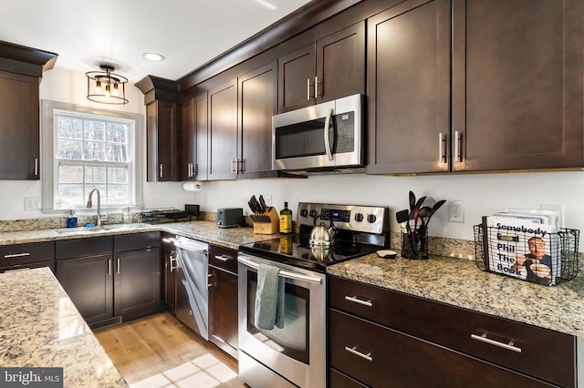 kitchen with appliances with stainless steel finishes, a sink, light stone counters, and dark brown cabinets