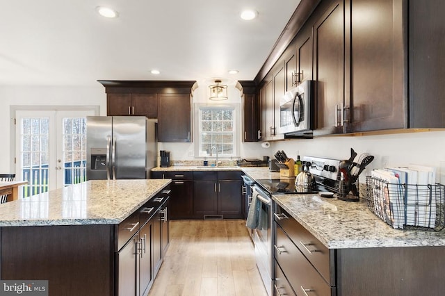 kitchen with light stone counters, french doors, appliances with stainless steel finishes, light wood-style floors, and a sink