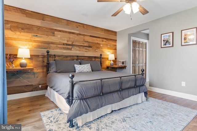 bedroom featuring wooden walls, a ceiling fan, baseboards, light wood-style floors, and a closet