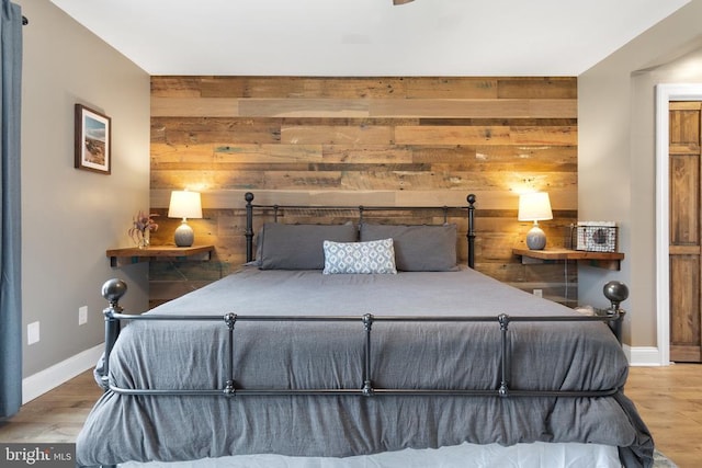 bedroom featuring an accent wall, wood walls, light wood-style flooring, and baseboards