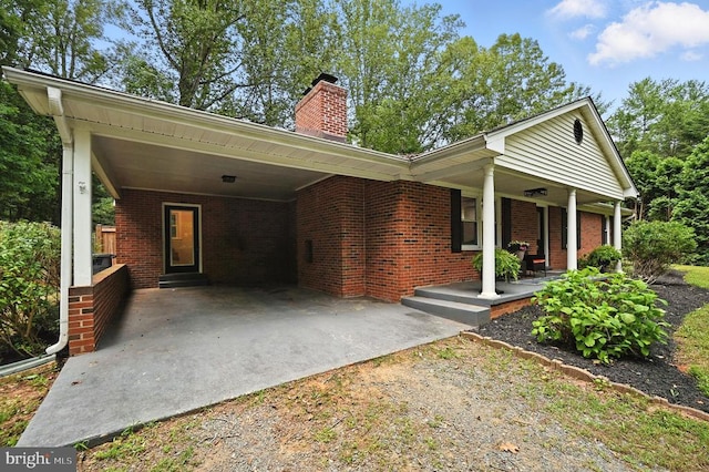  - view of front facade featuring driveway, covered porch, a carport, and brick siding
