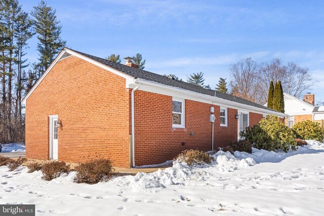 view of snowy exterior featuring brick siding and a chimney