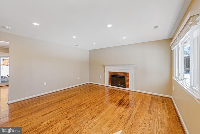 unfurnished living room with light wood-type flooring, visible vents, a fireplace, and baseboards