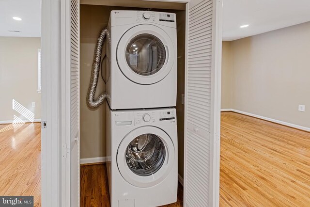 laundry area with recessed lighting, laundry area, wood finished floors, baseboards, and stacked washing maching and dryer