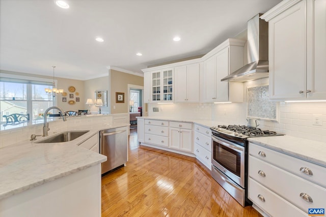 kitchen featuring appliances with stainless steel finishes, wall chimney range hood, a sink, crown molding, and white cabinets