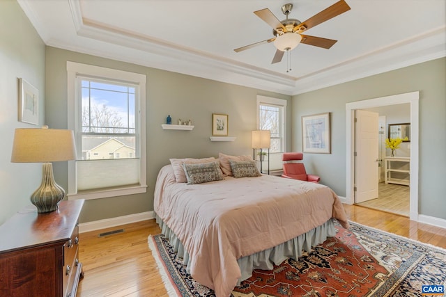 bedroom featuring a raised ceiling, ornamental molding, multiple windows, and light wood finished floors