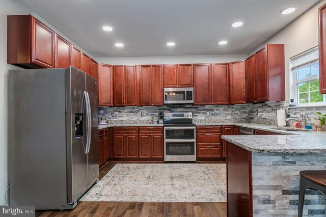  - kitchen featuring appliances with stainless steel finishes, wood finished floors, dark brown cabinets, tasteful backsplash, and recessed lighting