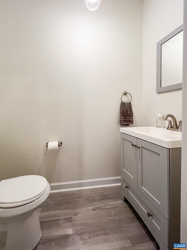 half bath featuring baseboards, wood finished floors, vanity, and toilet