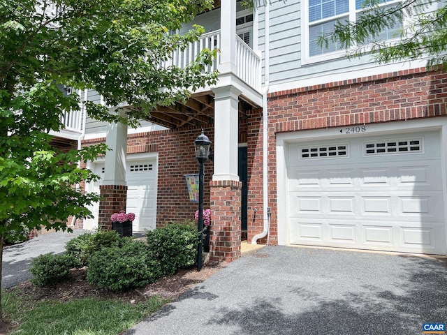 view of home's exterior with a garage, brick siding, a balcony, and asphalt driveway