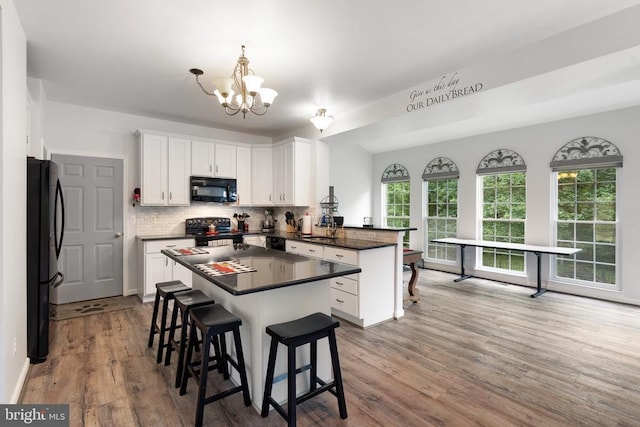  - kitchen featuring black appliances, a peninsula, dark countertops, backsplash, and wood finished floors