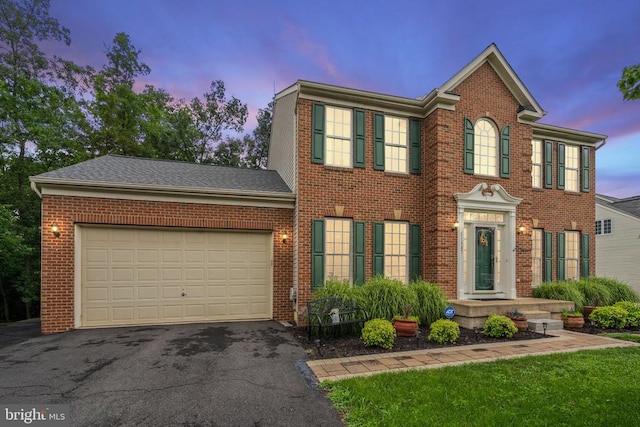  - colonial-style house featuring brick siding, asphalt driveway, and a garage