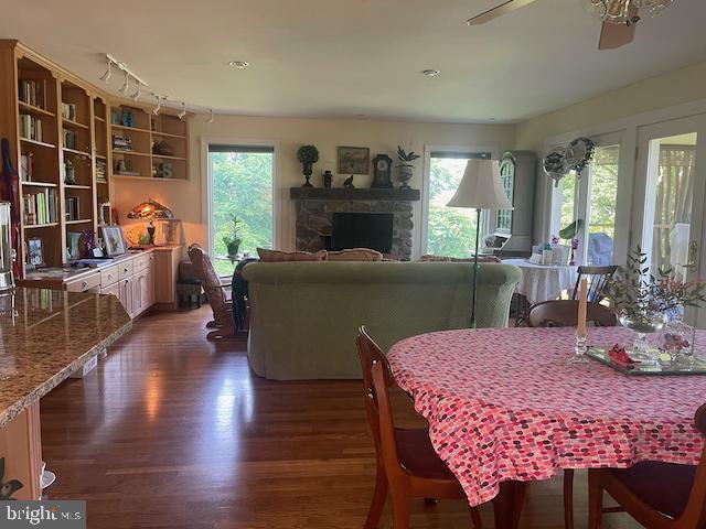  - dining area featuring dark wood-style flooring, plenty of natural light, ceiling fan, and a stone fireplace
