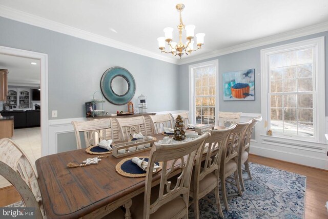 dining space featuring a chandelier, a wainscoted wall, ornamental molding, light wood-type flooring, and a decorative wall