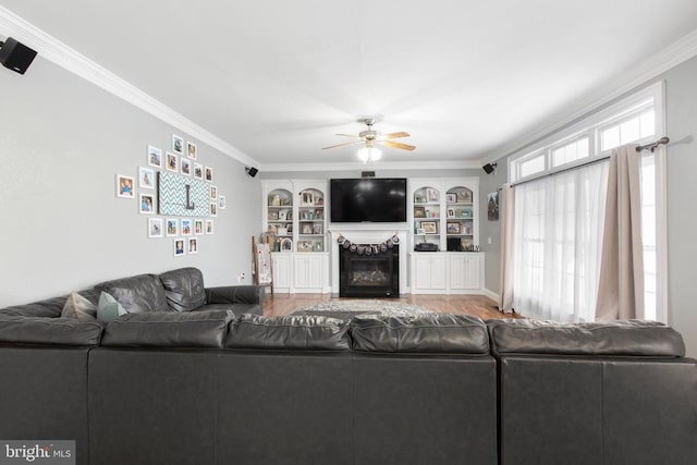 living room featuring ceiling fan, ornamental molding, wood finished floors, a glass covered fireplace, and built in features
