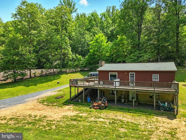  - rear view of house with a deck, gravel driveway, a yard, a chimney, and a forest view