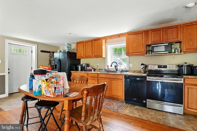  - kitchen featuring black appliances, a sink, light wood-style floors, and brown cabinetry