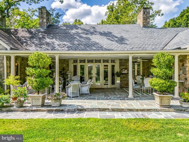 back of property featuring french doors, a chimney, stone siding, and a high end roof