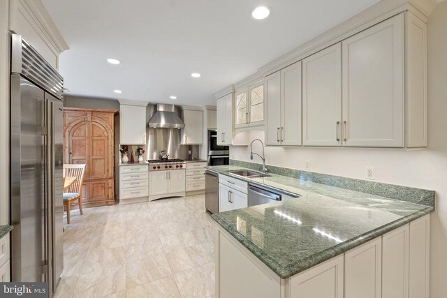 kitchen with stainless steel appliances, a sink, wall chimney range hood, recessed lighting, and a peninsula