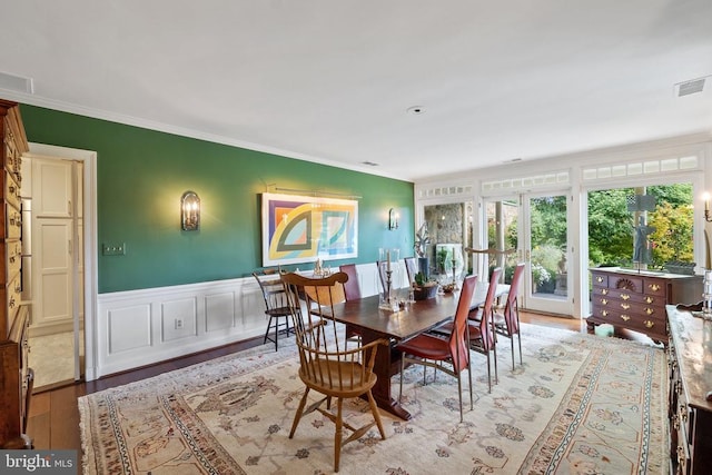 dining room featuring light wood-type flooring, crown molding, wainscoting, and a decorative wall