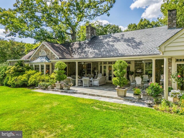 back of house with a chimney, stone siding, a lawn, and a patio area