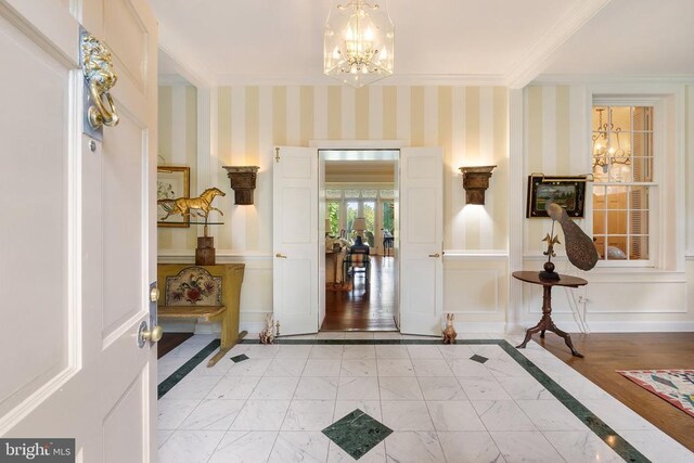 entrance foyer featuring a chandelier, crown molding, inlaid floor details, and light marble finish flooring