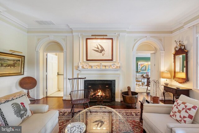 living area featuring ornamental molding, wood finished floors, arched walkways, and a high end fireplace