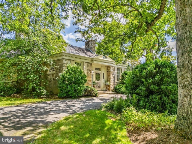 view of front facade featuring stone siding, a chimney, and driveway