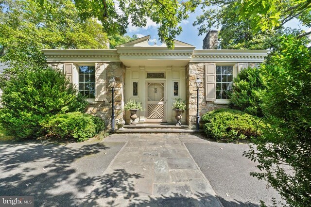 doorway to property with stone siding and a chimney