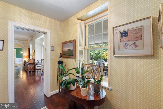 hall with dark wood finished floors, wallpapered walls, and baseboards