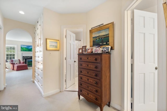 hallway featuring light colored carpet, arched walkways, and baseboards