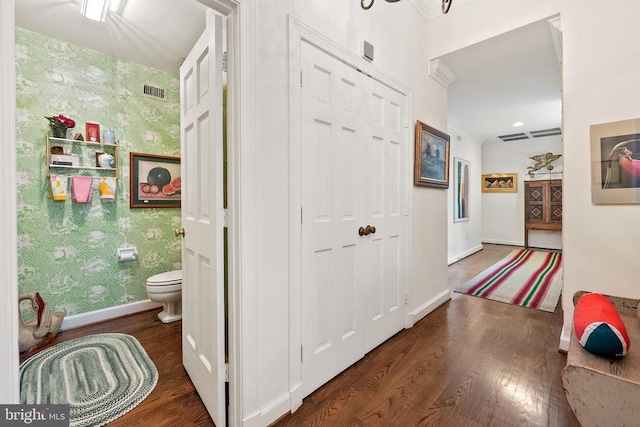 hall featuring wallpapered walls, wood finished floors, baseboards, and crown molding