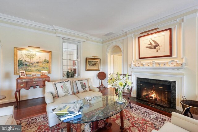 living room featuring crown molding, wood finished floors, a lit fireplace, and arched walkways