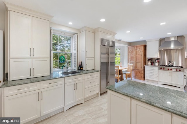 kitchen with wall chimney exhaust hood, stainless steel appliances, a sink, dark stone countertops, and recessed lighting